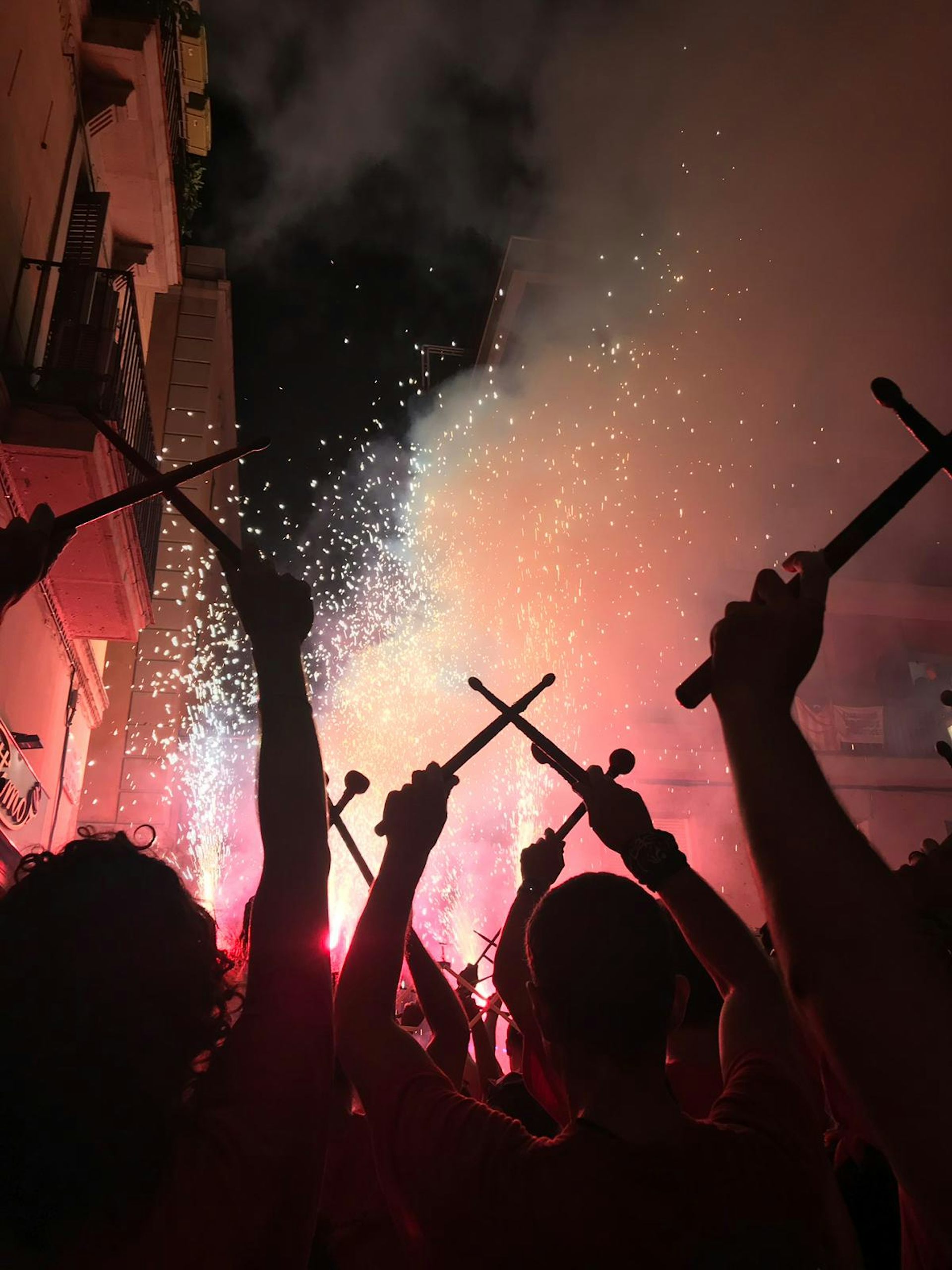 Grupo de tamborileros con tambores elevados sobre sus cabezas, con fuegos artificiales de fondo.