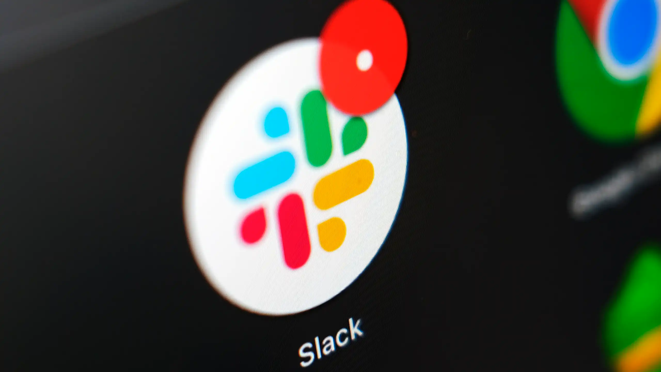 A Slack icon, with its trademark blue, green, yellow and red pattern, is displayed against a dark screen with a message notification on its upper right.