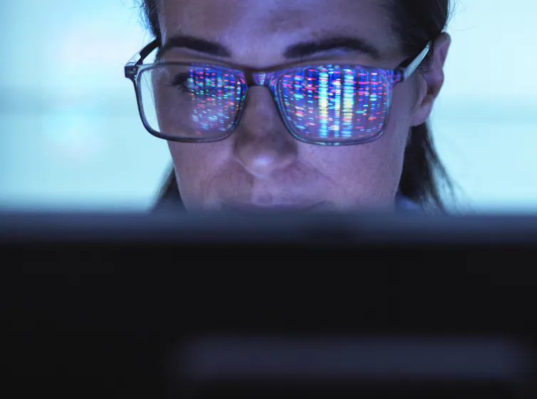 Close-up of face of person viewing computer screen, colorful DNA sequence reflected on their glasses