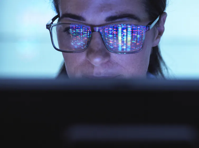 Close-up of face of person viewing computer screen, colorful DNA sequence reflected on their glasses