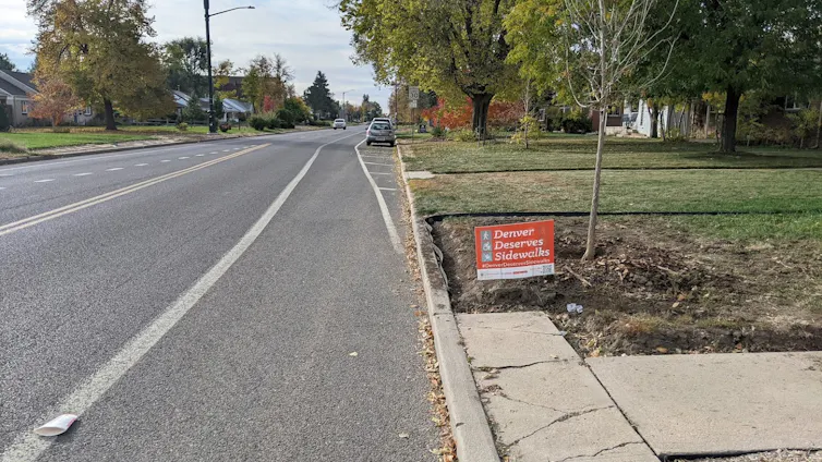 A yard sign that says 'Denver Deserves Sidewalks.'