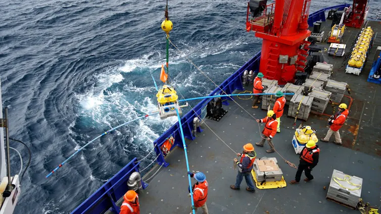 People aboard a ship lower a large instrument into the water.