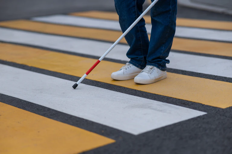 Blind person crossing the road, using a white cane.