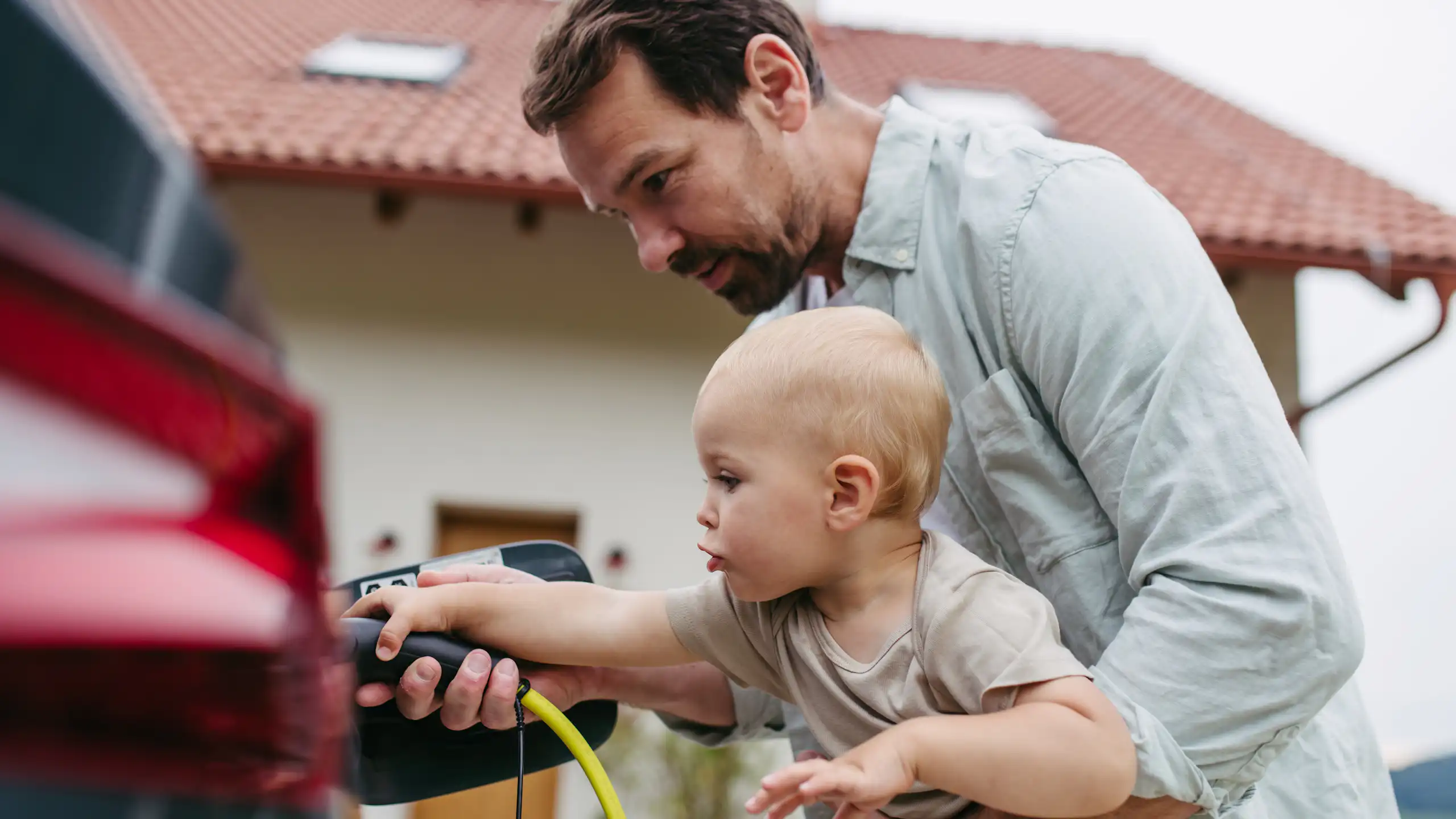 man holding toddler and teaching him to plug in his electric vehicle.