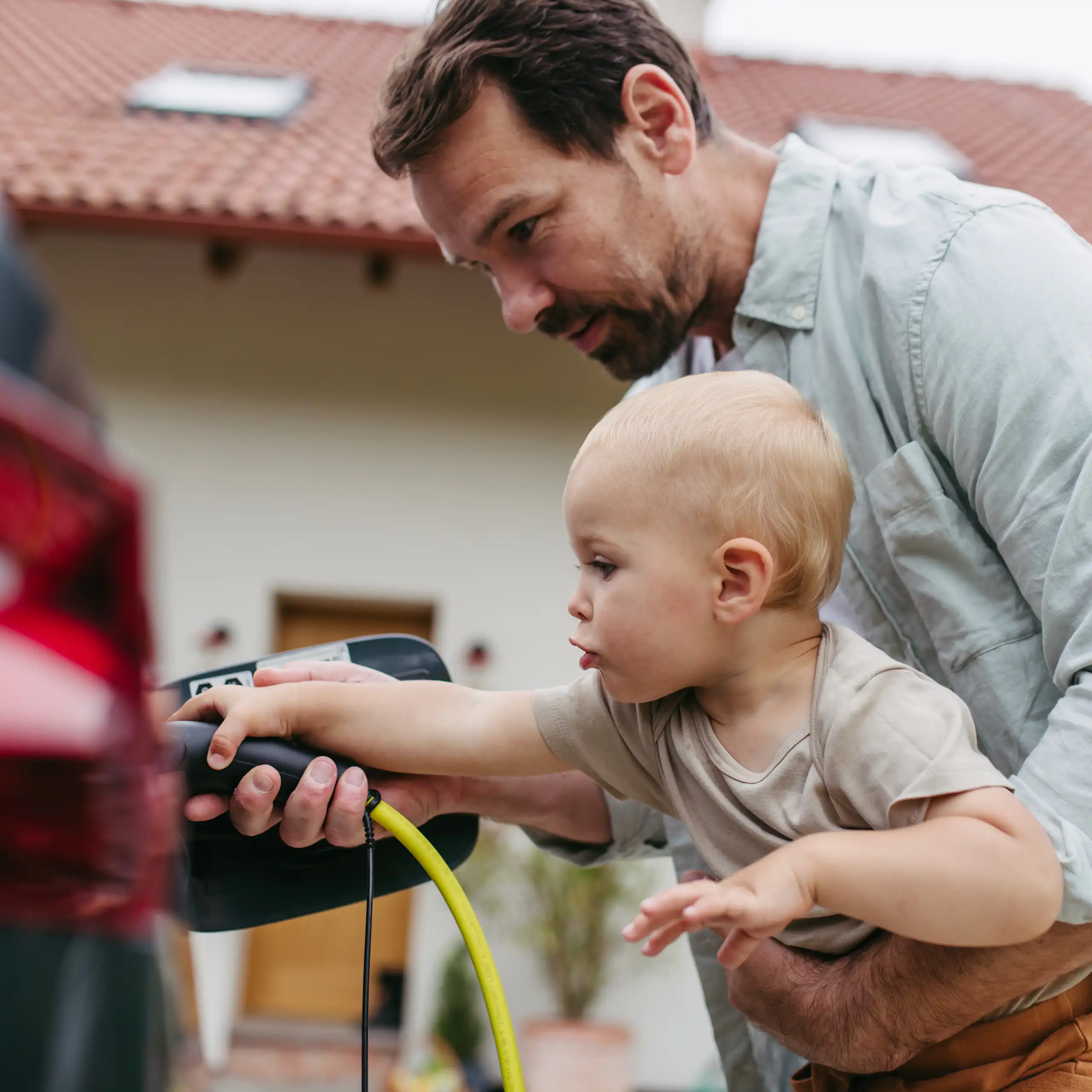 man holding toddler and teaching him to plug in his electric vehicle.