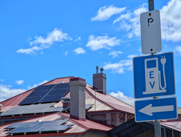 sign pointing to EV charger, house with solar on roof in background.