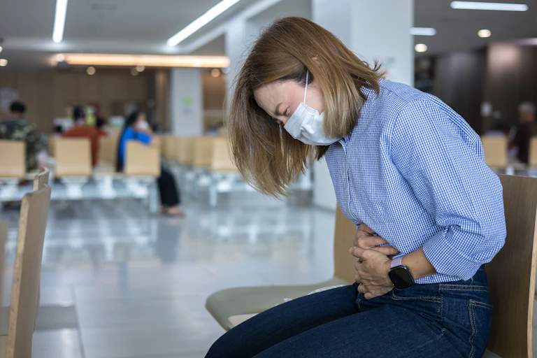 Woman waiting to be seen in hospital, bent over double in pain.