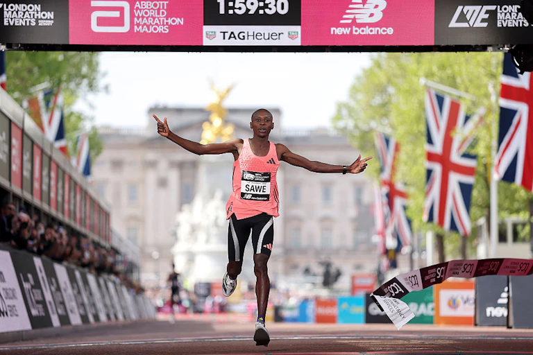 A man running, arms spread out, at a finishing line showing 1:59:30