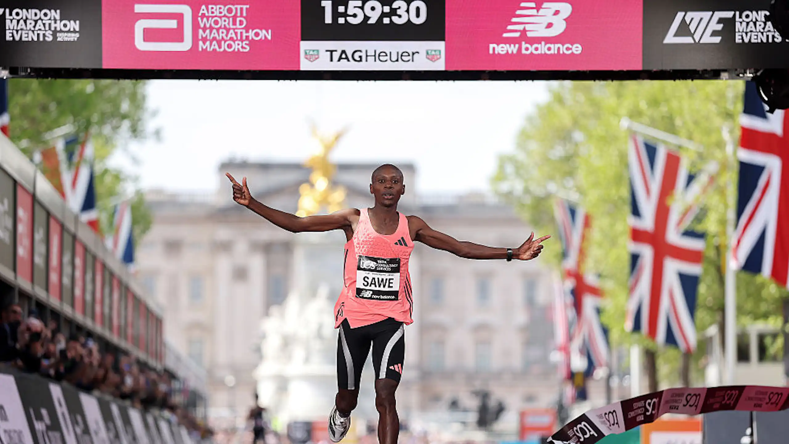A man running, arms spread out, at a finishing line showing 1:59:30