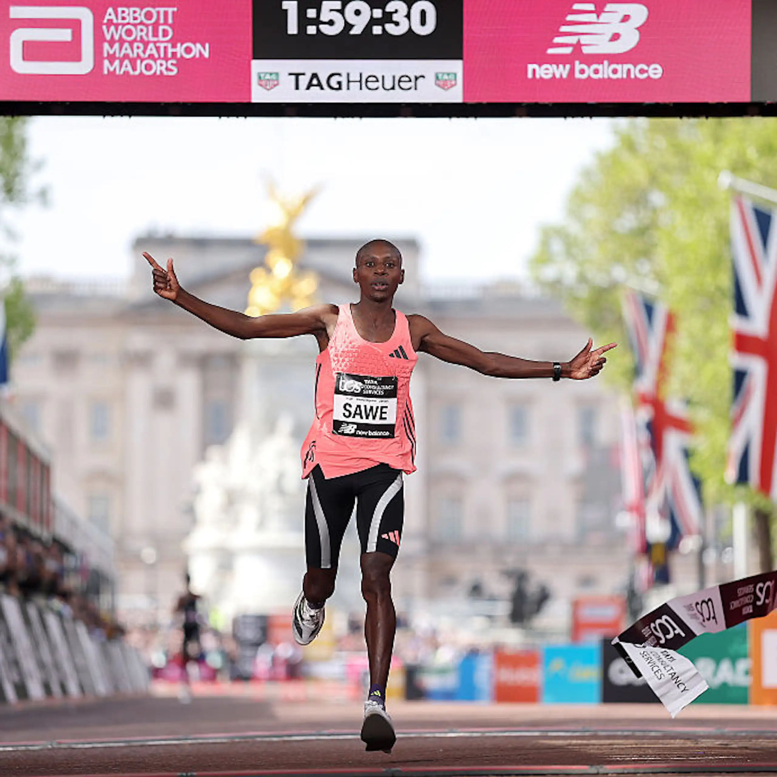 A man running, arms spread out, at a finishing line showing 1:59:30