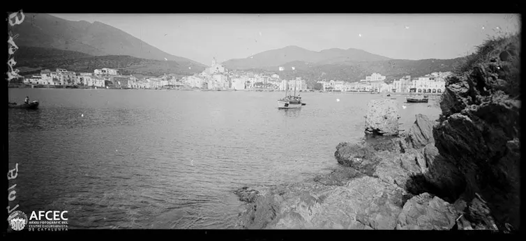 Fotografia en blanc i negre d'una badia amb un poble costaner de fons.