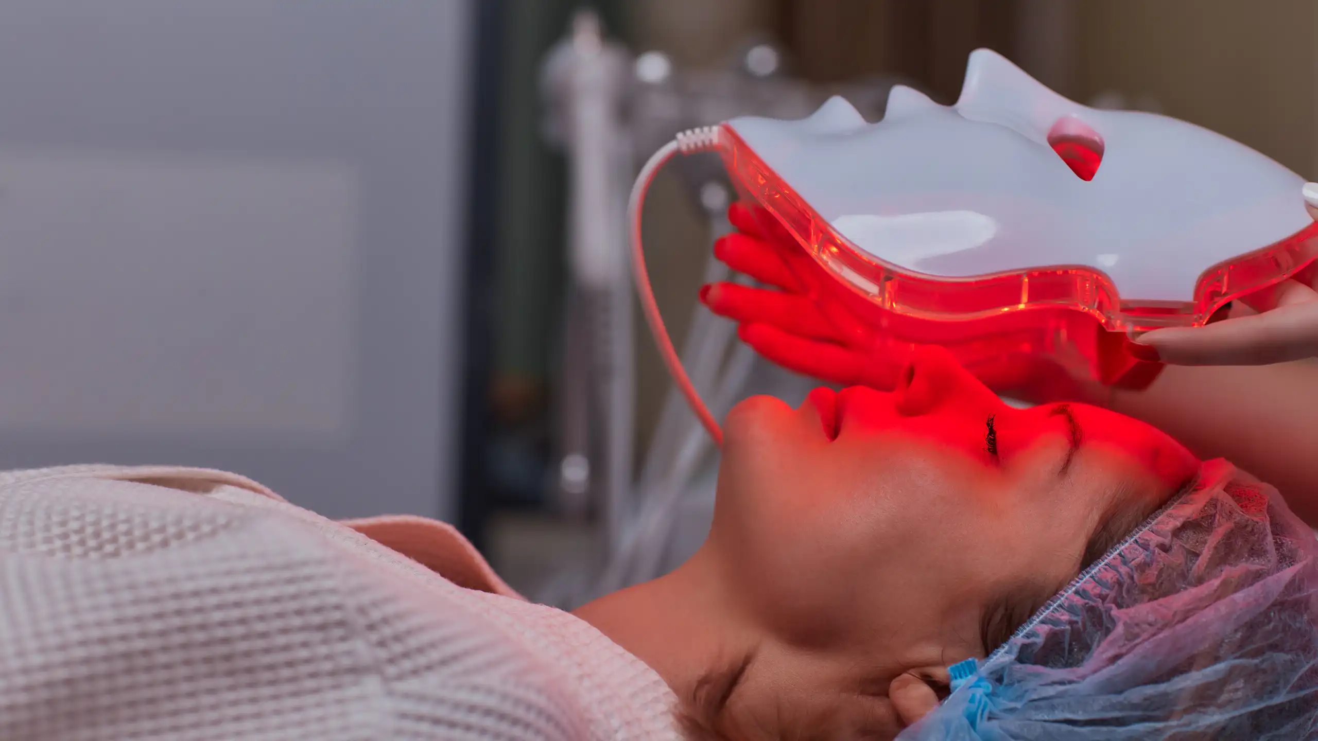 Un masque à lumière rouge est déposé sur le visage d'une femme.