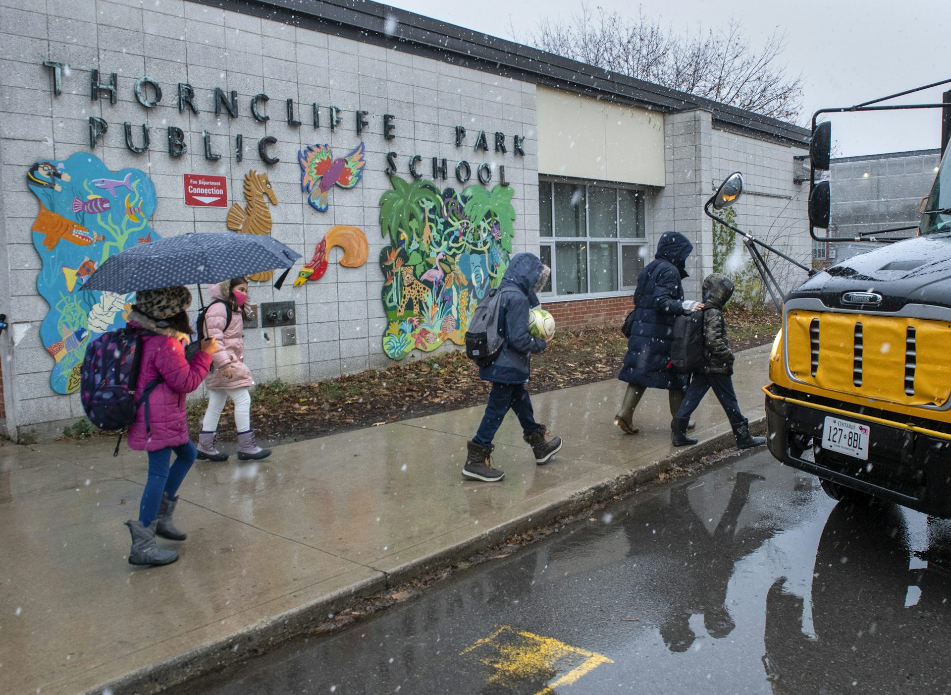 Estudiantes con paraguas vistos en la acera cerca del autobús escolar.