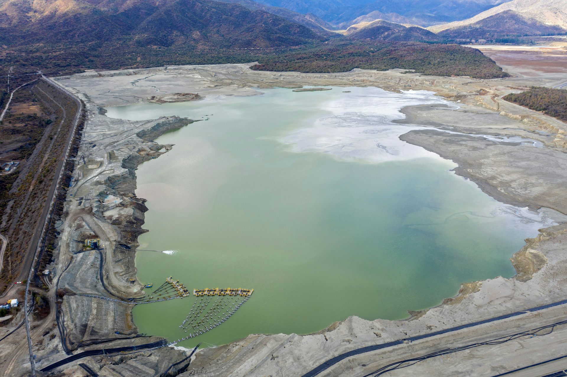 Un gran lago con bordes irregulares, caminos a sus lados y montañas al fondo.