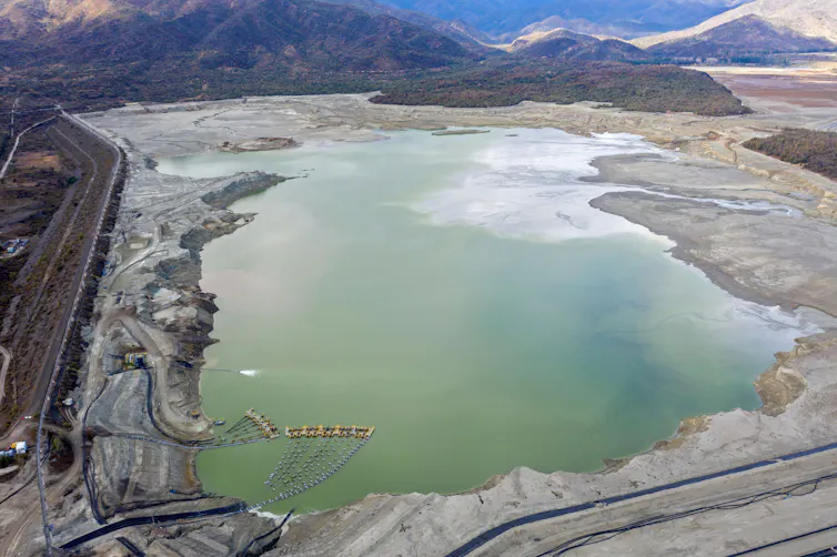 La carrera por extraer minerales críticos para la inteligencia artificial y la energía limpia está creando "zonas de sacrificio" que dañan el agua y la salud de los pobres del mundo. 3 Un gran lago con bordes irregulares, caminos a sus lados y montañas al fondo.