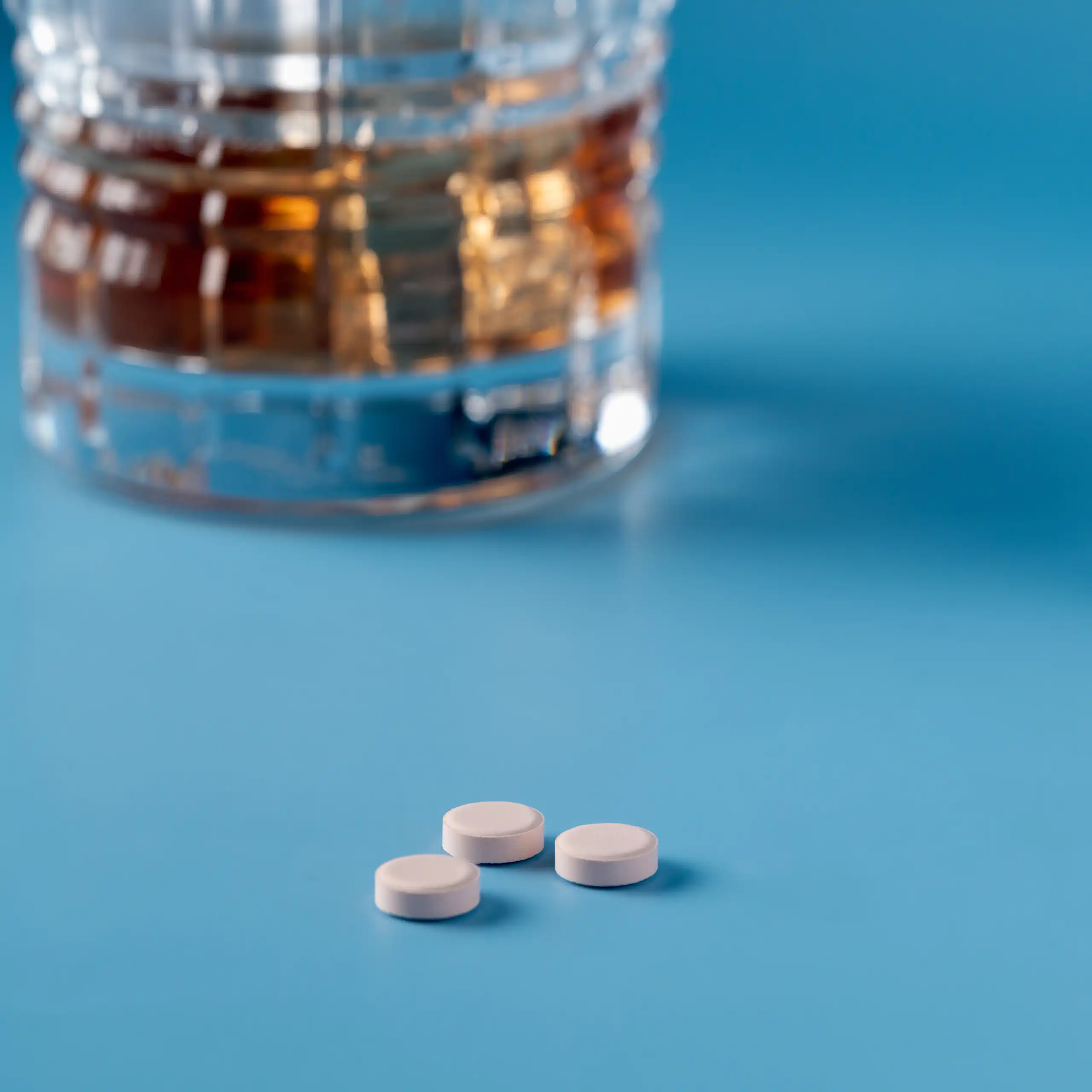 Photo d’un verre d’alcool posé à côté de médicaments, sur une table de couleur bleue.