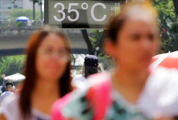 two women walking down street, road sign in background says 35degrees indicating hot weather