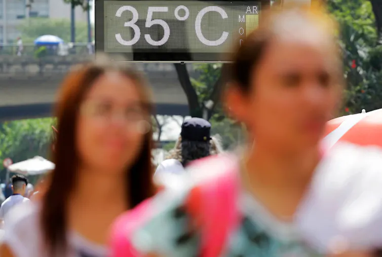 two women walking down street, road sign in background says 35degrees indicating hot weather