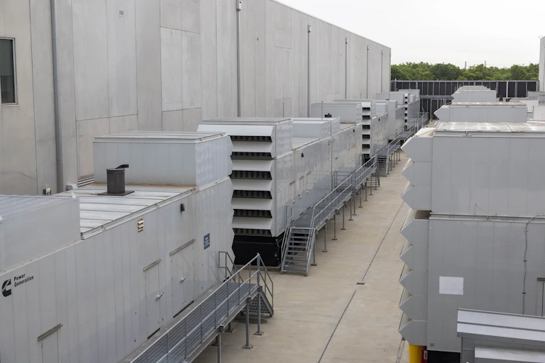 A group of large metal boxes are lined up next to a concrete building.