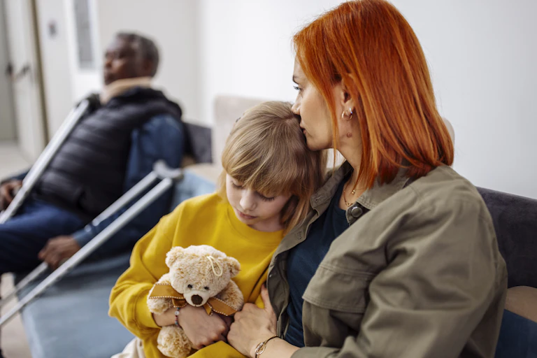 Woman sits in waiting room next to her child, who is holding a teddy