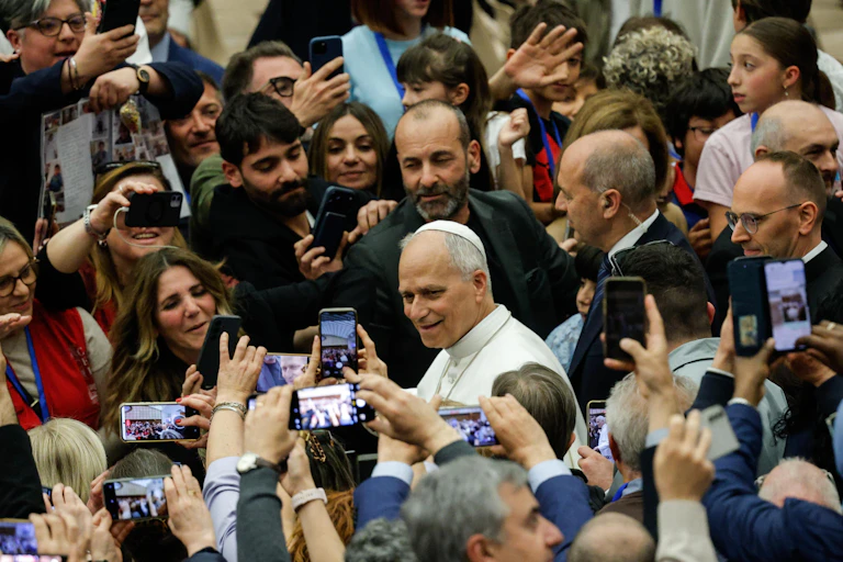 Pope Leo XIV surrounded by crowds of people taking photos of him