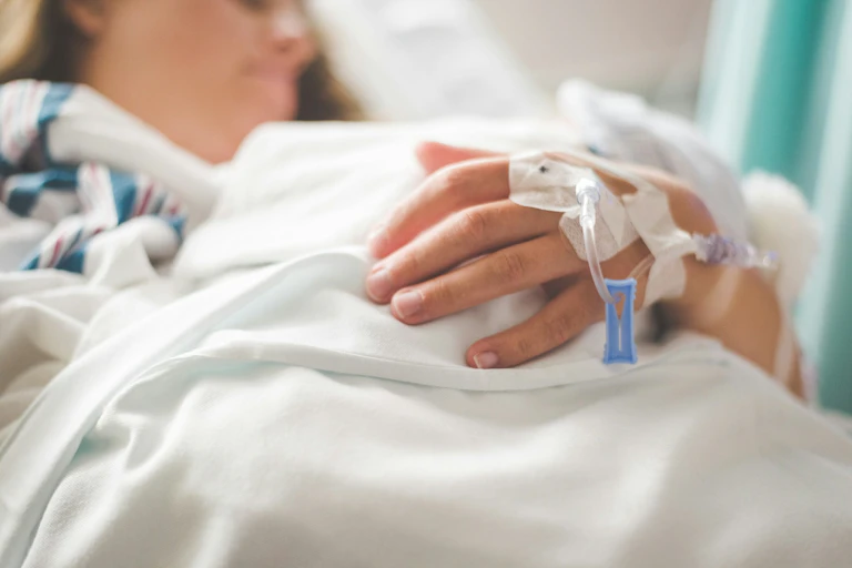 Woman lying in hospital bed, with needles in arm