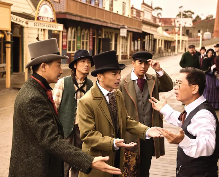 Production still: some dapper men argue on a historic street.