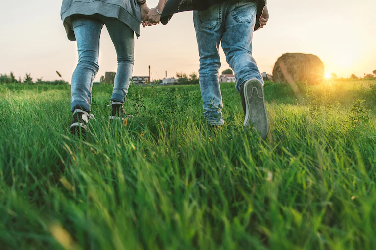 Las piernas de dos adolescentes en un campo verde al atardecer.