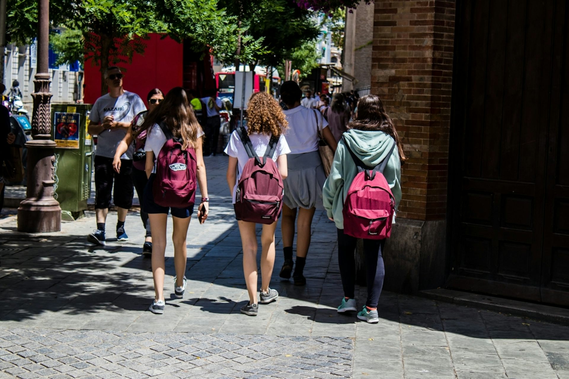Tres adolescentes caminan por la acera con mochilas a la espalda.