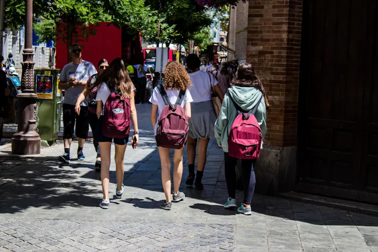 Tres adolescentes caminan por una acera con las mochilas a la espalda.