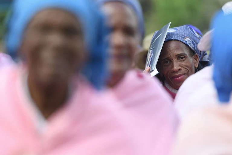 Group of elderly women wearing blue head wraps, out of focus except for one face