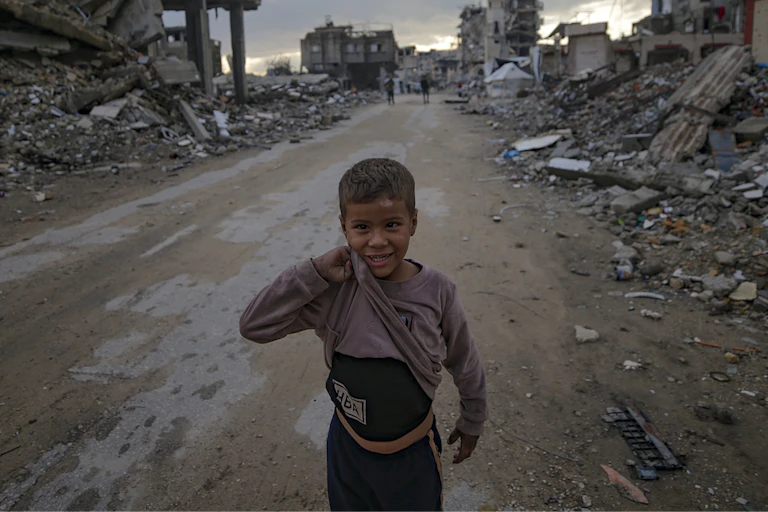 A little boy stands in the middle of a street filled with destroyed buildings.