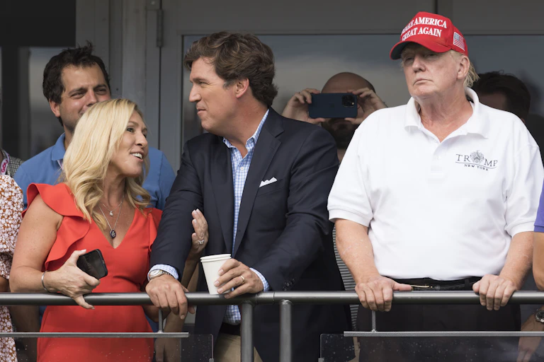 Majorie Taylor Greene and Tucker Carlson stand alongside Donald Trump.