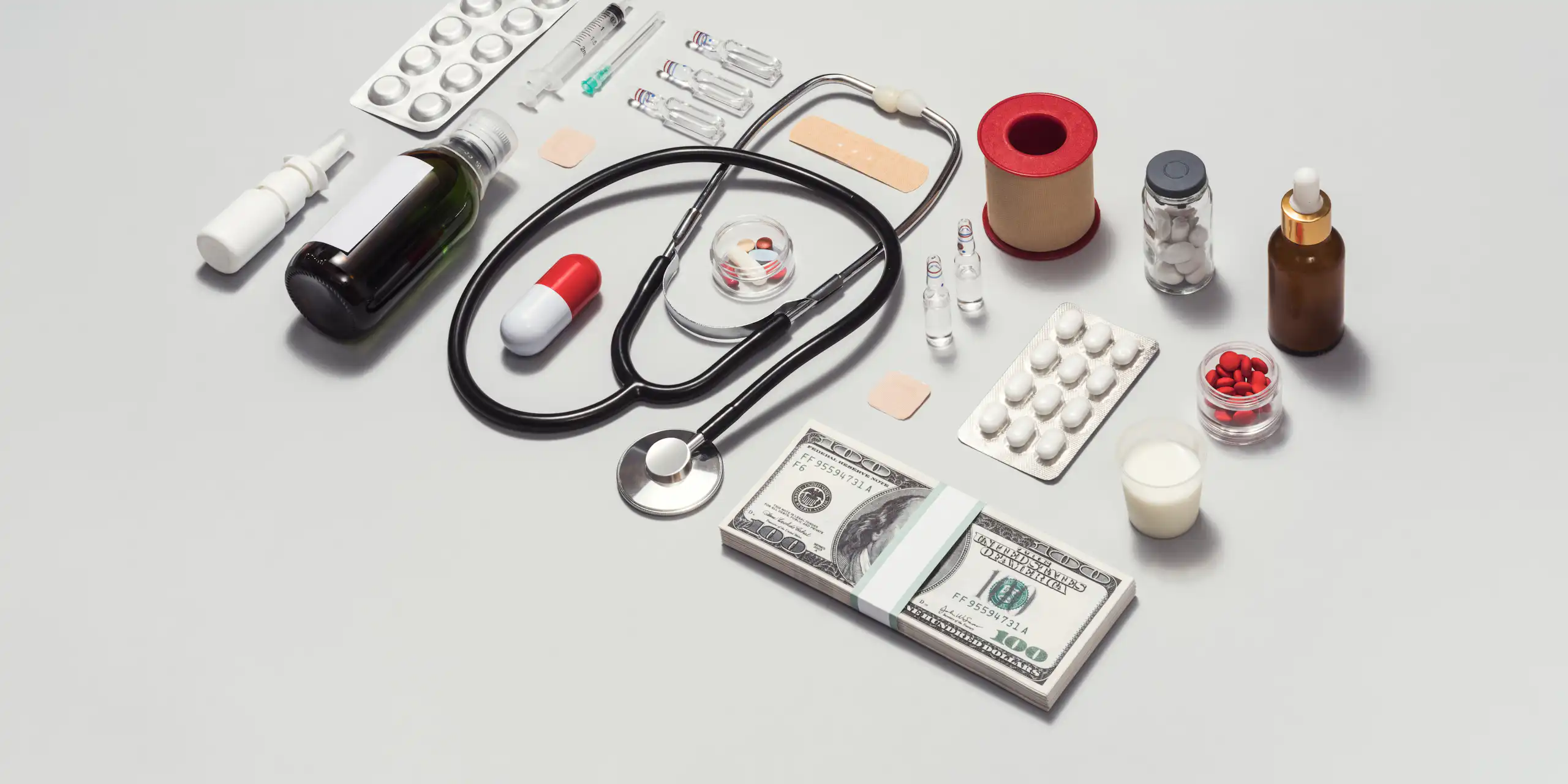 Various medical supplies arrayed in a neat rectangle, a stack of $100 bills on the bottom right corner