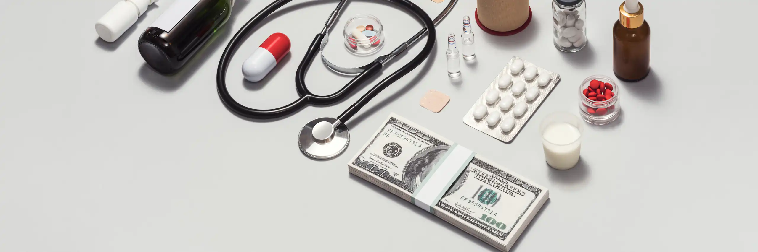 Various medical supplies arrayed in a neat rectangle, a stack of $100 bills on the bottom right corner