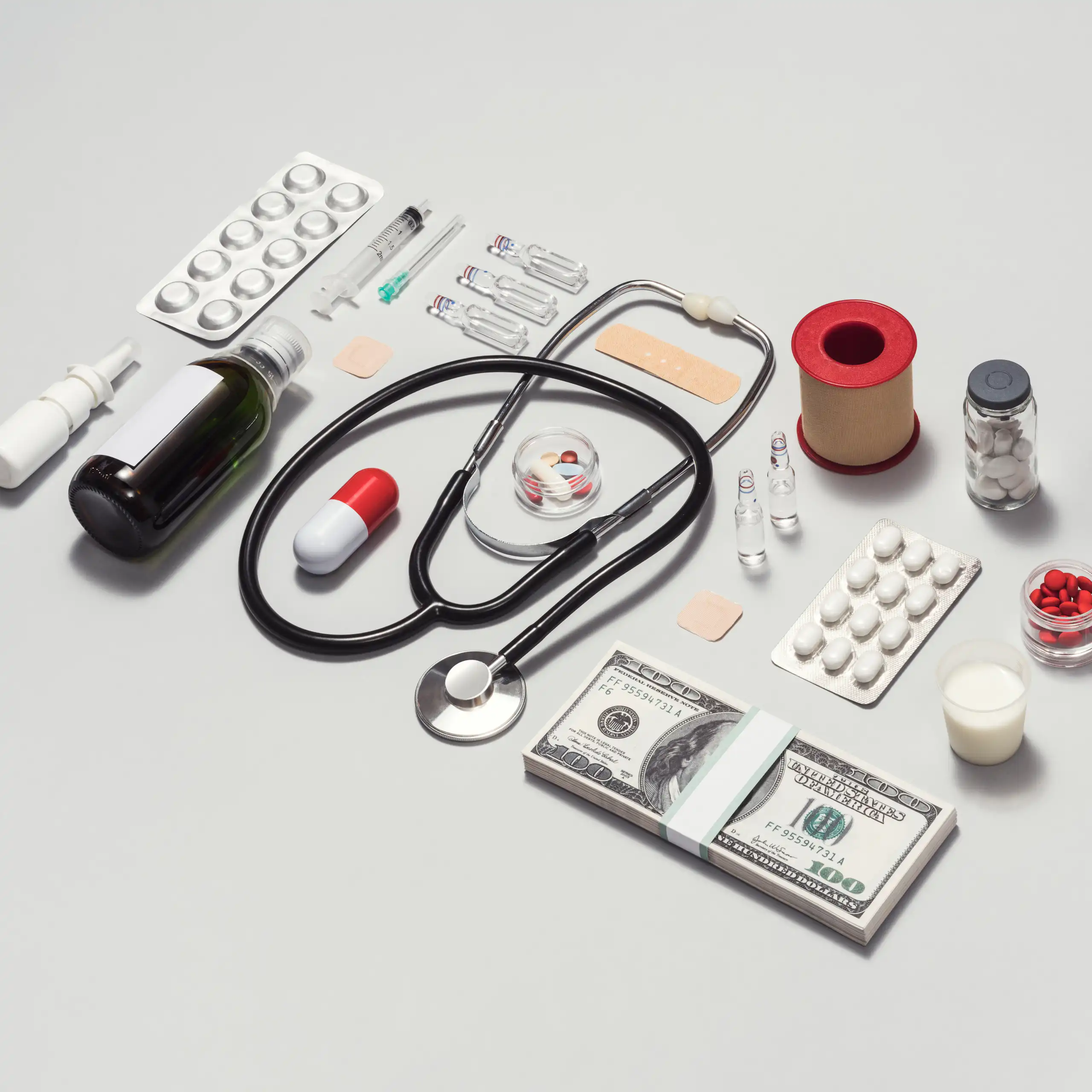 Various medical supplies arrayed in a neat rectangle, a stack of $100 bills on the bottom right corner