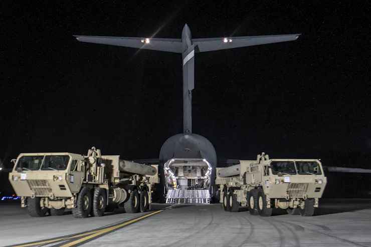 Tanks and military equipment appear in front of a military plane.