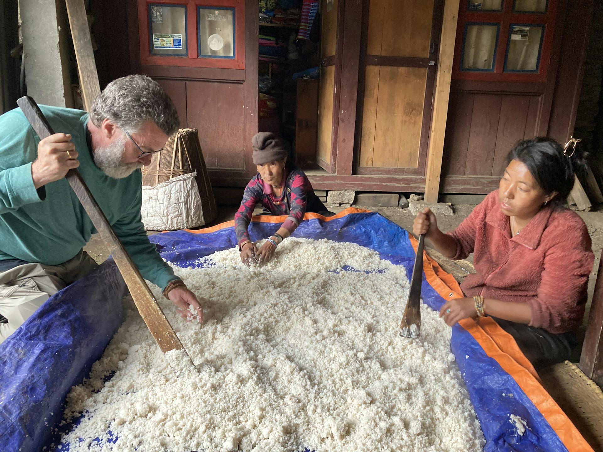 Three people use wooden spatulas to stir rice.