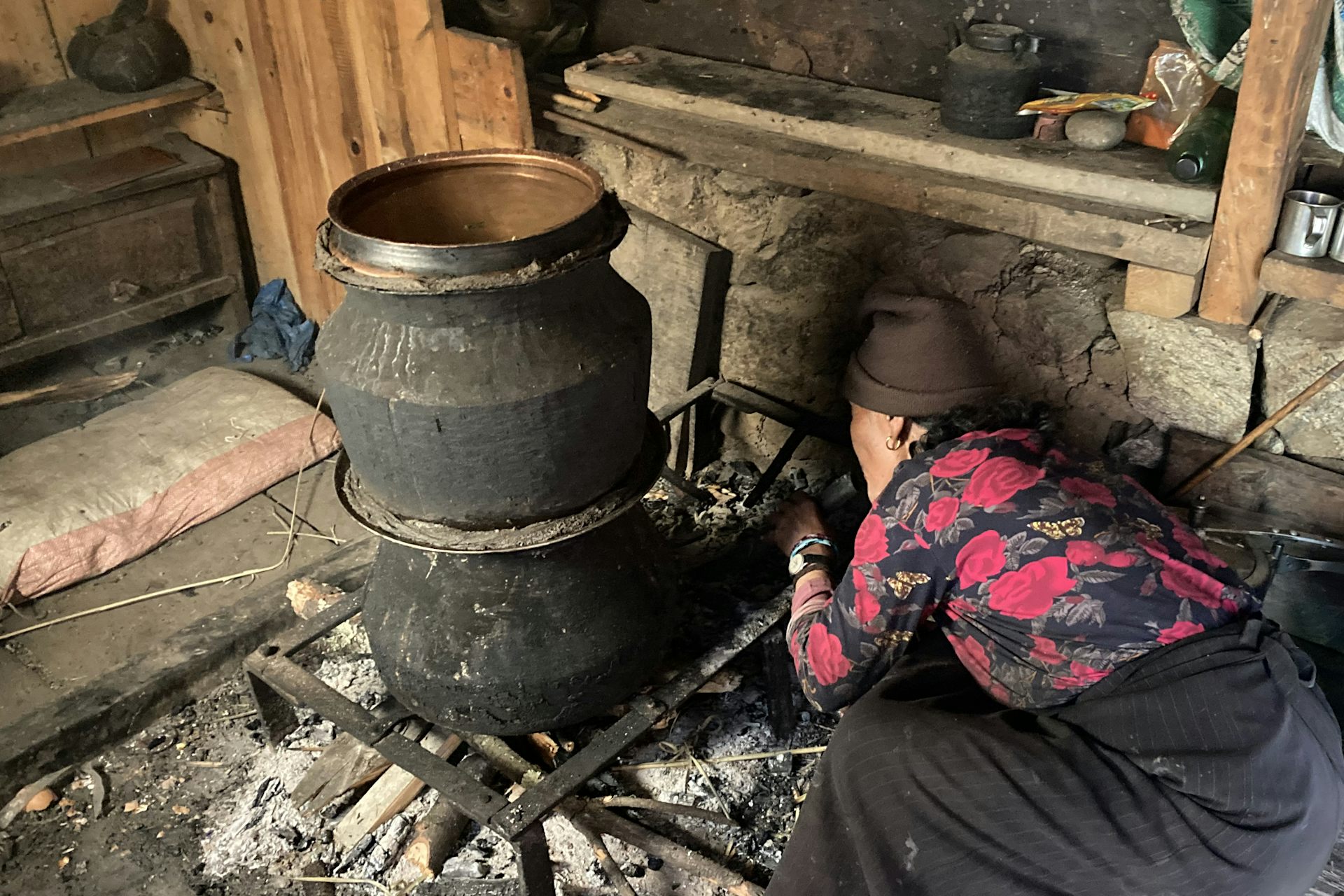 A woman pokes a fiew under a big pot.