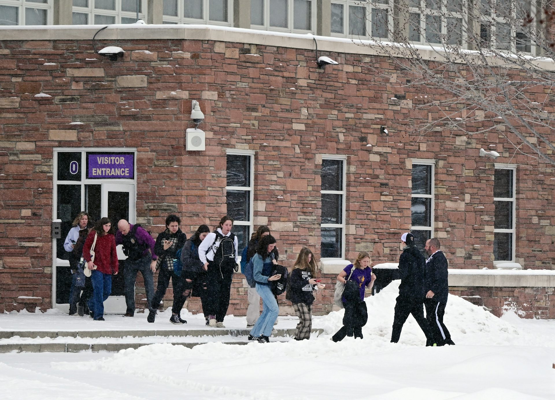 Se ve a un grupo de personas saliendo de un edificio de ladrillo y caminando sobre un césped nevado.