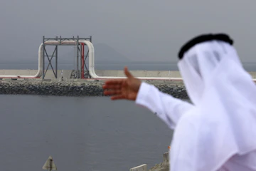 A man in traditional Emirati dress looks out to a large oil pipeline.