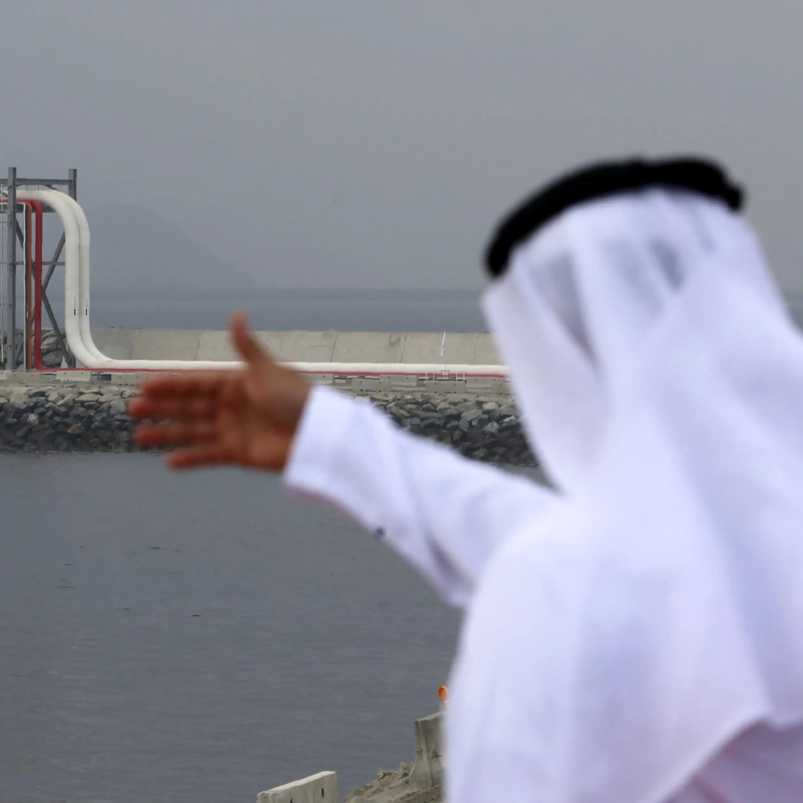 A man in traditional Emirati dress looks out to a large oil pipeline.