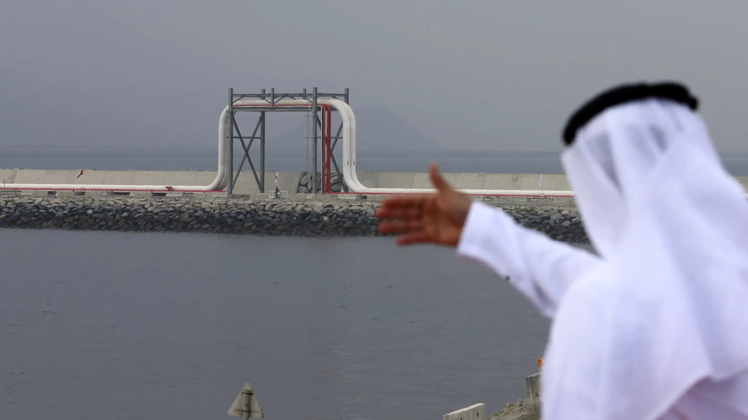 A man in traditional Emirati dress looks out to a large oil pipeline.