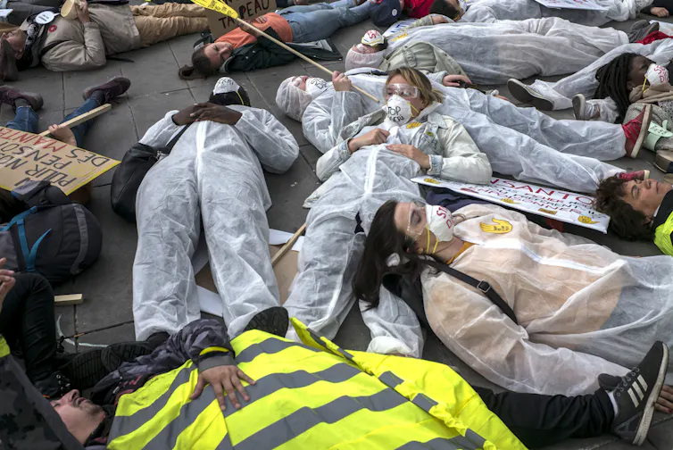 People wearing protective clothing lie down in the street.