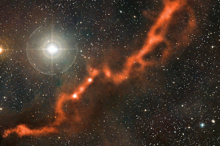 Céu repleto de estrelas com uma nebulosa alaranjada que se estende da parte inferior esquerda até a parte superior direita da imagem