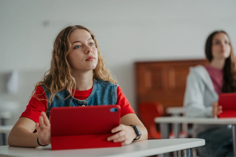 A teenage student listening attentively in class with a tablet.
