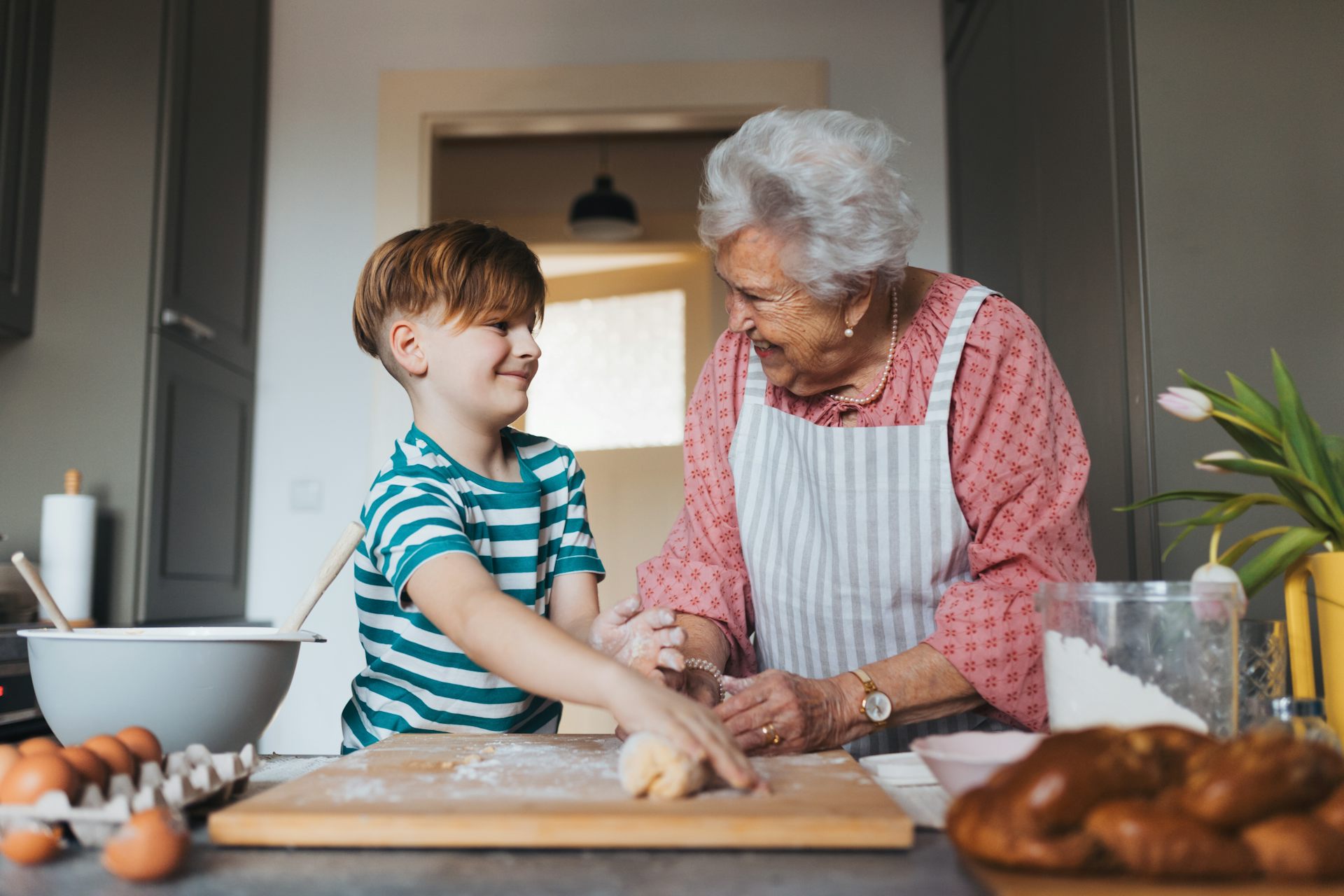 A grandma prepares a dough for bread with her young grandson.