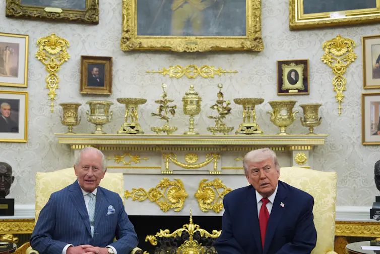 Two older men sit in an office strewn with gold decor.