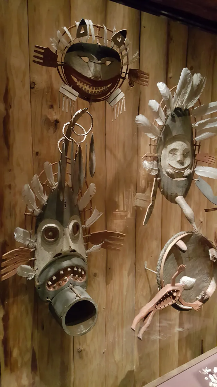 A series of brown masks of faces is seen mounted against wood