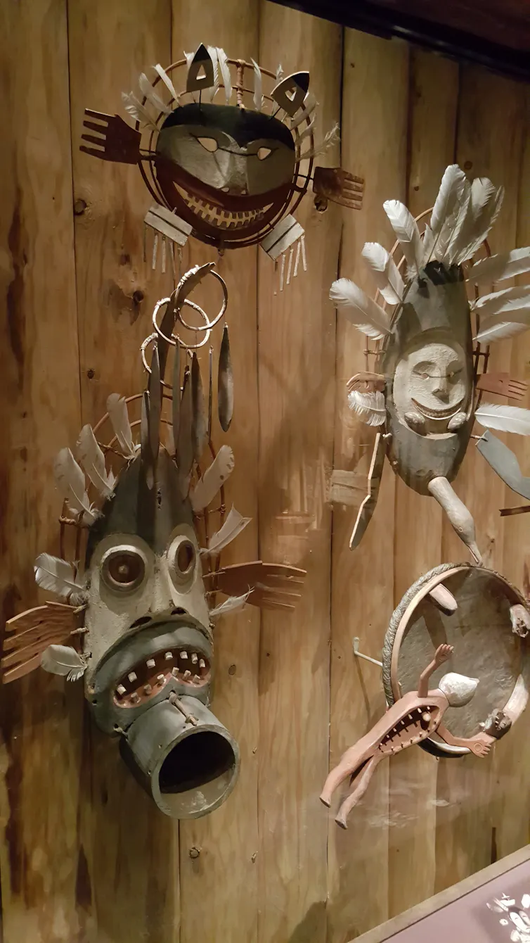 A series of brown masks of faces is seen mounted against wood